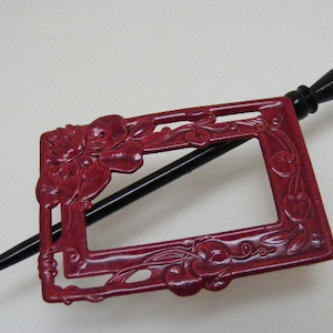 May include: A red and black hair stick with a decorative floral design. The stick is made of metal and has a black wooden handle.