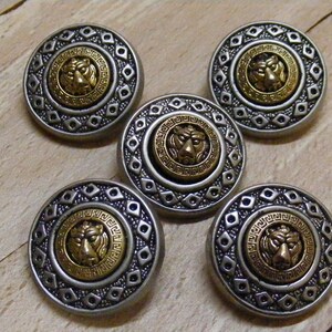 May include: Five silver and gold buttons with a lion head design in the center. The buttons have a decorative border with a geometric pattern.