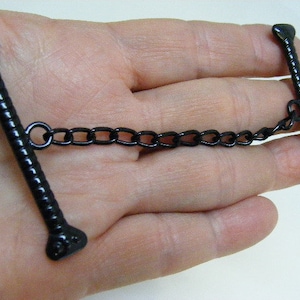 May include: Black metal toggle clasp with a chain connector. The clasp has a twisted design and rounded ends.