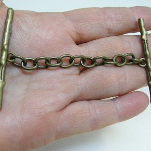 May include: A bronze-colored chain with two decorative, twig-like clasps. The clasps have a textured, wood-like finish.