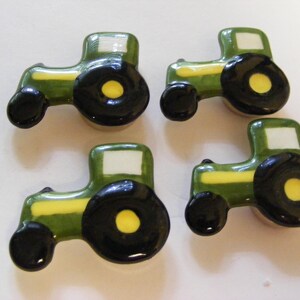 May include: Four ceramic tractor-shaped knobs in a glossy finish. Each piece features a dark green body, a yellow stripe along the side, a white square window, and large black wheels with yellow centers. The design is uniform across all four items.