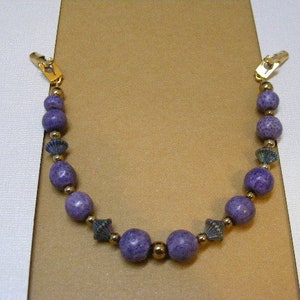 May include: A purple and gold beaded necklace with a clasp on each end. The beads are round and have a textured surface.