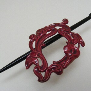 May include: A red metal hair stick with a floral design. The stick is black and has a rounded end.
