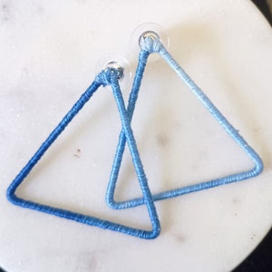 May include: A pair of ombre blue triangle earrings. The earrings are made of a soft, woven material and have a silver tone post.