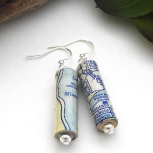 May include: A pair of earrings made from rolled up maps. The earrings are silver and have a blue and white map design. The map text includes "12th St", "11th St", "Lake Minnetonka", "University", "Minne", "Shar Mar Nursing Home", "Abriendo", "Longwood", "Dunsmeare".