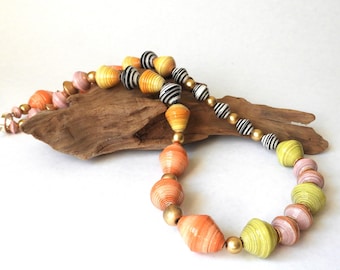 May include: A long necklace made of colorful paper beads. The beads are layered in shades of pink, orange, yellow, and black. The necklace is accented with gold beads.