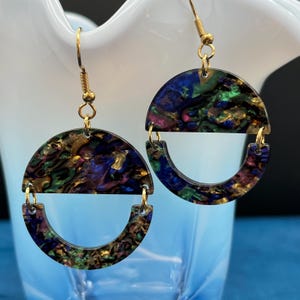 May include: A pair of gold hoop earrings with a semi-circle of iridescent green, blue, and purple resin. The resin has a marbled effect with gold flecks.