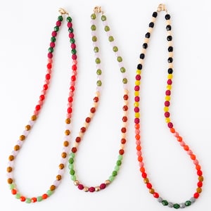 May include: Three beaded necklaces with gold clasps are displayed against a white background. The necklaces feature a variety of colorful beads, including red, green, yellow, and orange. The beads are arranged in a gradient pattern.