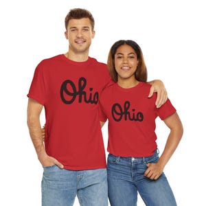 May include: Two red t-shirts with black "Ohio" lettering in a stylized font. The shirts are worn by two people standing side-by-side.