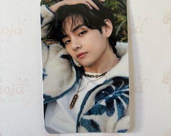 May include: A rectangular photo card with a person with dark hair and a light complexion. The person is wearing a white jacket with blue and white patterned accents. The card has rounded corners and the text "moja by K" is visible.