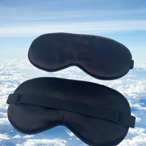 May include: Two black sleep masks, one with an adjustable strap. The masks are made of a soft, silky material and are designed to block out light.
