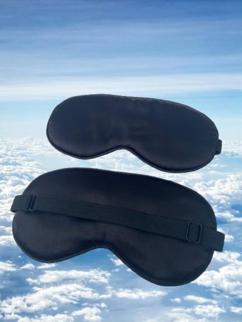 May include: Two black sleep masks, one with an adjustable strap. The masks are made of a soft, silky material and are designed to block out light.