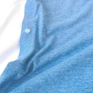 May include: A light blue button-down shirt with a textured fabric. The shirt has a few light blue buttons down the front and a white background.