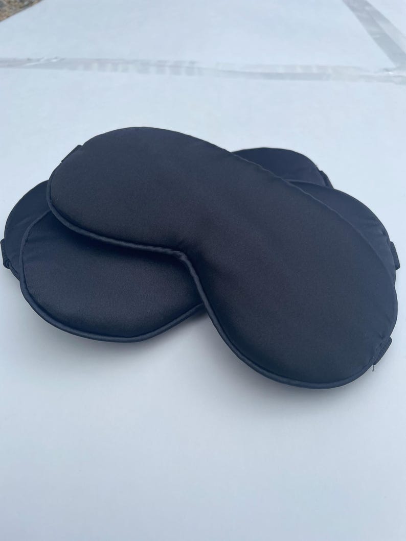 May include: Two black sleep masks made of soft, silky fabric. The masks are designed to block out light and help you sleep.