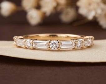 May include: A gold band ring featuring an alternating pattern of clear baguette-cut and round-cut stones set in a row. The ring has a polished metal finish and is positioned horizontally. The logo Luxcraft Jewels is visible in the bottom right corner.