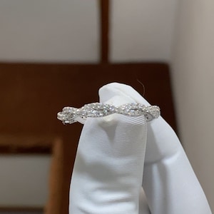 Puede incluir: Un delicado anillo de banda de oro blanco con un diseño trenzado, adornado con diamantes brillantes.
