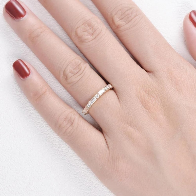 May include: A delicate gold band with a row of baguette and round diamonds. The ring is on a person's finger.
