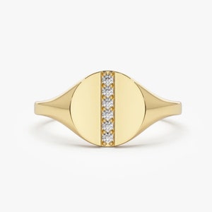 May include: A gold signet ring with a smooth oval top and a single row of small diamonds down the center.