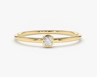 May include: A simple gold band ring with a single round bezel-set diamond.