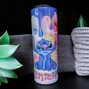 May include: A blue and white stainless steel tumbler with a colorful design featuring Stitch from Lilo & Stitch. The design includes flowers, leaves, and the word "Stitch" in pink letters.