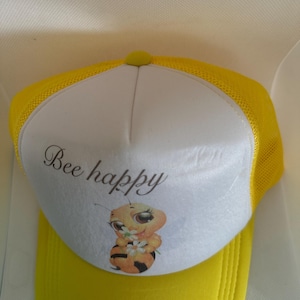 May include: A yellow and white trucker hat with a cartoon bee and the text "Bee happy".