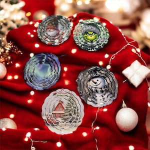May include: A collection of Christmas ornaments with festive designs. The ornaments feature images of a gnome, the Grinch, a winter scene, a snowman, and a red barn. They are displayed on a red surface with string lights and other ornaments.