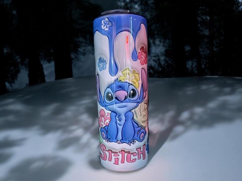 May include: A blue and white stainless steel tumbler with a cartoon image of Stitch from Lilo & Stitch. The tumbler has a pink, blue, and yellow floral design and the word "Stitch" is written in pink letters at the bottom.