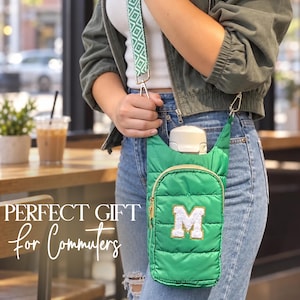 May include: A bright green quilted water bottle carrier featuring a gold zipper, a white letter M patch with gold trim, and a detachable green and white patterned shoulder strap. The bag holds a white water bottle and is worn across the body.