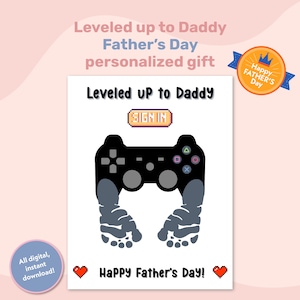 Könnte beinhalten: Eine digitale druckbare Karte mit einem schwarzen und grauen Videospiel-Controller mit zwei grauen Fußabdrücken als Griffe. Die Karte lautet "Leveled up to Daddy" und "Happy Father's Day!" in Pixel-Schrift.