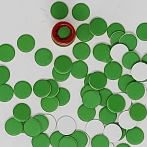 Pode incluir: Uma coleção de peças de jogo circulares verdes e brancas espalhadas sobre uma superfície branca. Uma única peça de jogo vermelha e castanha está centrada. As peças, pequenas e uniformes, sugerem um jogo de tabuleiro.