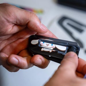 May include: A black plastic utility knife featuring a graphic of a white cartoon character with long ears, blue eyes, and a pink mouth. The tool has a sliding mechanism on the top and a textured black wheel on the side for blade adjustment.