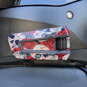 May include: A black motorcycle helmet communication device featuring a vibrant graphic overlay of skulls and red roses. The device is mounted on the side of a matte black helmet, which displays the text VZ160 SHARK FOR RACING USE ONLY.