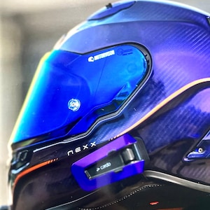 May include: A Nexx motorcycle helmet featuring a deep blue and purple carbon fiber shell with orange accents. The helmet includes a reflective blue visor with Motorvisor branding and a Cardo communication device attached to the side.
