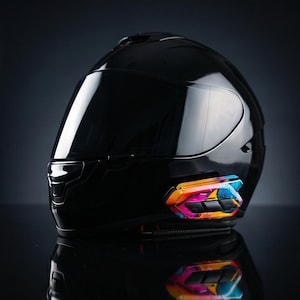 Könnte beinhalten: Ein glänzender schwarzer Integralhelm für Motorräder mit einem dunkel getönten Visier. An der Seite ist ein Kommunikationsgerät mit einem lebendigen, mehrfarbigen abstrakten Farbspritzmuster in Pink, Blau, Orange und Gelb angebracht.