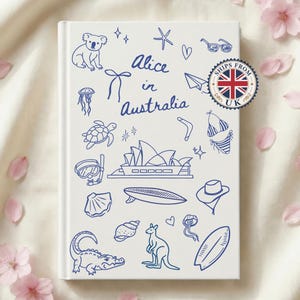 May include: A white hardback book titled Alice in Australia featuring blue line art illustrations of a koala, kangaroo, crocodile, Sydney Opera House, surfboard, and various sea life. A circular sticker with a UK flag is attached to the cover.