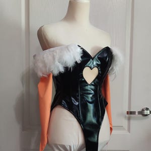 May include: Black bodysuit with a heart-shaped cutout and white feather trim. The costume has orange sleeves and is displayed on a mannequin. The bodysuit is made of a shiny material.