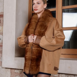 Peut inclure: Un manteau beige avec un col et des poignets en fourrure marron. Le manteau a une fermeture à boutons et un détail en cuir sur les manches. Un style classique, adapté au temps froid.