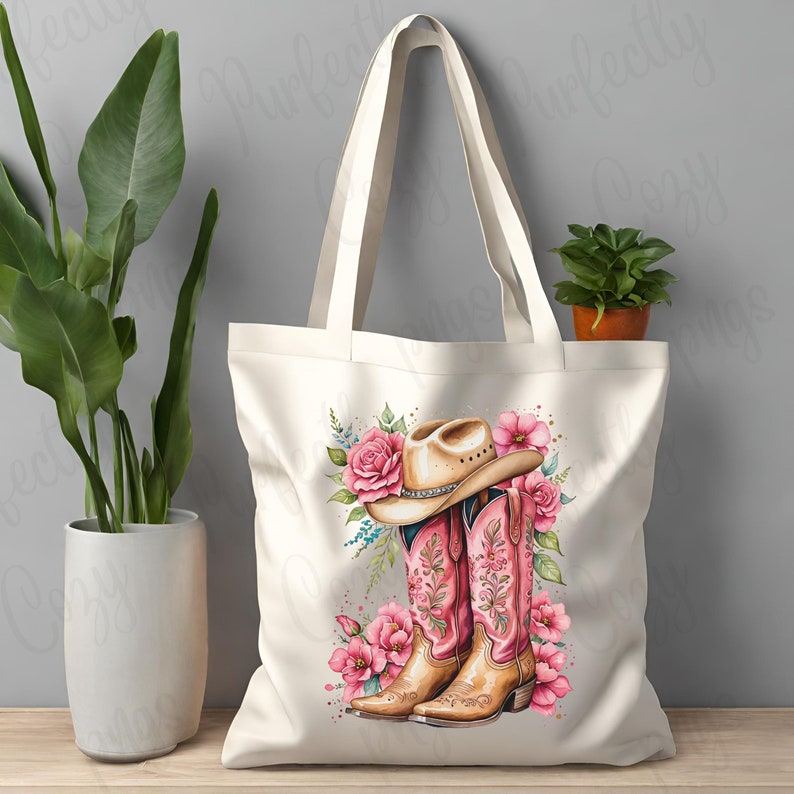 K&ouml;nnte beinhalten: Eine wei&szlig;e Canvas-Tragetasche mit einem Design aus rosa und braunen Cowboystiefeln und einem Hut. Das Design enth&auml;lt rosa Blumen und gr&uuml;ne Bl&auml;tter.