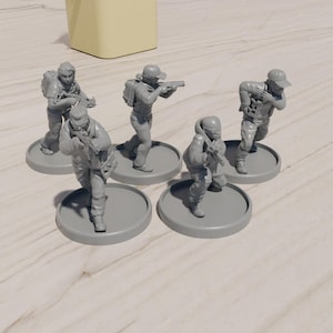Può includere: Una collezione di cinque figurine grigie in miniatura di soldati in varie pose d'azione, ognuna con un fucile. Le figure sono montate su basi circolari, probabilmente per un gioco da tavolo o un set di modelli.