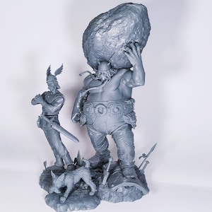 Op de afbeelding: Een grijs 3D-geprint beeldje van een grote, gespierde Viking die een grote rots boven zijn hoofd houdt. Een kleiner Vikingbeeldje staat links van de grotere figuur en houdt een zwaard vast. Een klein hondenbeeldje staat voor de grotere Viking.