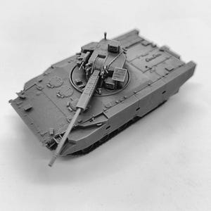 Puede incluir: Un modelo de tanque gris con un largo cañón que se extiende desde la torreta. El tanque tiene un cuerpo rectangular con detalles, incluyendo escotillas y otros componentes. La imagen está tomada desde un ángulo alto.