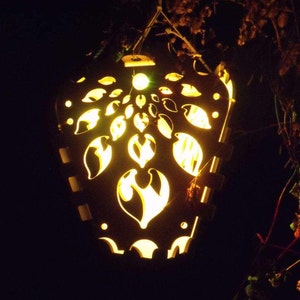 Op de afbeelding: Een decoratieve lantaarn met een uitgesneden ontwerp van bladeren en bloemen. De lantaarn wordt van binnenuit verlicht en geeft een warm gloed.