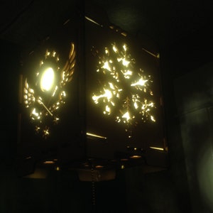 Op de afbeelding: Een houten lampenkap met een uitgesneden sneeuwvlokkenpatroon. De lampenkap wordt van binnenuit verlicht, waardoor een warme gloed ontstaat.