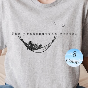 May include: Gray t-shirt with the text "The prosecution rests." and a graphic of a person relaxing in a hammock. The graphic is in black and white. The t-shirt is available in 8 colors.