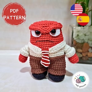 Puede incluir: Juguete amigurumi de crochet del personaje Ira de la película Del revés. El juguete es rojo con una camisa blanca, pantalones marrones y una corbata roja y blanca a rayas. El juguete tiene una expresión de enfado con el ceño fruncido y una mueca.