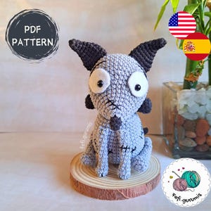 Puede incluir: Un perro gris tejido a mano con grandes ojos blancos y detalles negros. Está sentado sobre una rodaja de madera. La imagen incluye el texto "PDF PATTERN" en un diseño circular.