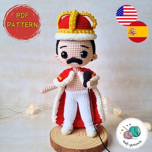 Puede incluir: Muñeco de ganchillo de una figura con capa roja y blanca, pantalón blanco y corona dorada. El muñeco tiene bigote negro y sostiene un micrófono negro. La imagen incluye el texto "PDF PATTERN".