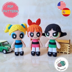 Puede incluir: Tres muñecas de ganchillo hechas a mano que representan a las Supernenas. Las muñecas tienen pelo amarillo, rojo y negro. Llevan trajes con rayas negras y ojos grandes. Incluye el texto "PDF PATTERN".