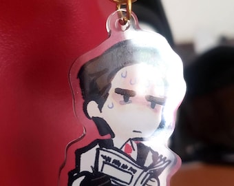 May include: A clear acrylic charm featuring a cartoon illustration of a man in a suit, holding a newspaper. The charm has a gold-colored keychain attachment. The man has a stressed expression.