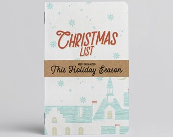 Puede incluir: Una libreta blanca con una ilustración azul y verde de un pueblo nevado. La libreta tiene el texto "Christmas List" en rojo y "Keep Organized This Holiday Season" en negro.